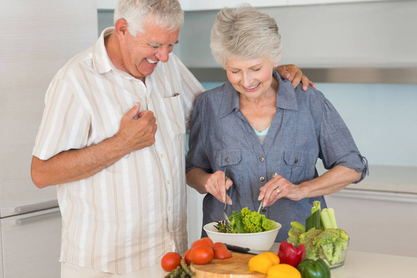 Smiling senior couple preparing a salad at home in the kitchen - 写真・画像