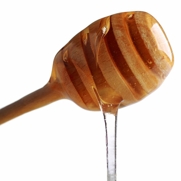 Honey dripping from a wooden honey dipper isolated on white background - 写真・画像
