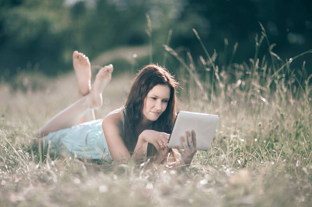 cute girl with digital tablet lying on lawn on summer day - Photo, Image