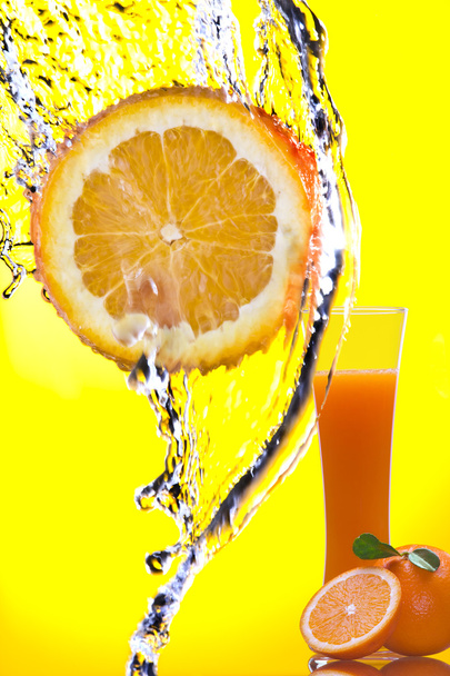 Blick auf ein Orangenstück, das bespritzt wird und ein Glas Saft auf dem Rücken - Foto, Bild