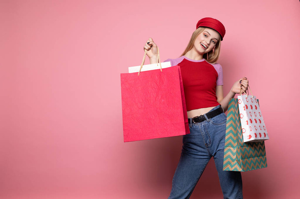 Atrakcyjna blondynka w luźnych ubraniach i czerwonym kapeluszu z kolorowymi torbami na zakupy - Zdjęcie, obraz