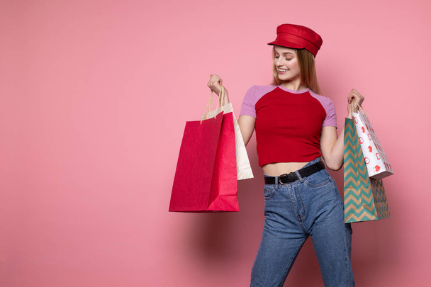 Привлекательная блондинка в повседневной одежде и красной шляпе с красочными пакетами для покупок
 - Фото, изображение