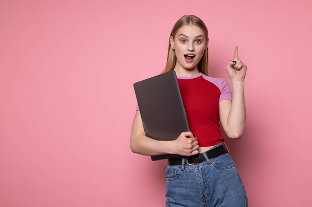 Opgewonden jong blond meisje in rode t-shirt houden laptop computer, kijken naar camera - Foto, afbeelding
