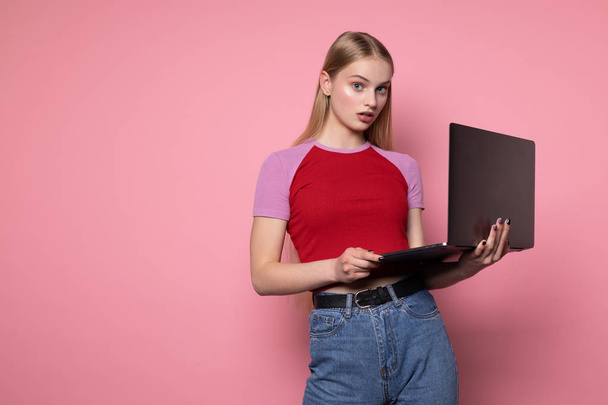 Portrait of surprised beautiful girl student in red t-shirt and blue jeans using laptop - Photo, Image