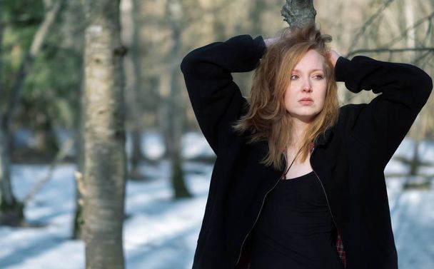 Jeune femme sexy en vêtements noirs, aux cheveux roux, à l'air triste, dans la forêt d'hiver
. - Photo, image