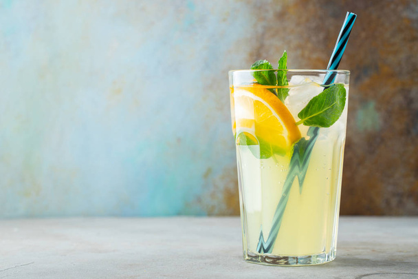 glas met limonade of Mojito cocktail met citroen en munt, koud verfrissend drankje of drank met ijs op een rustieke blauwe achtergrond. Ruimte kopiëren - Foto, afbeelding
