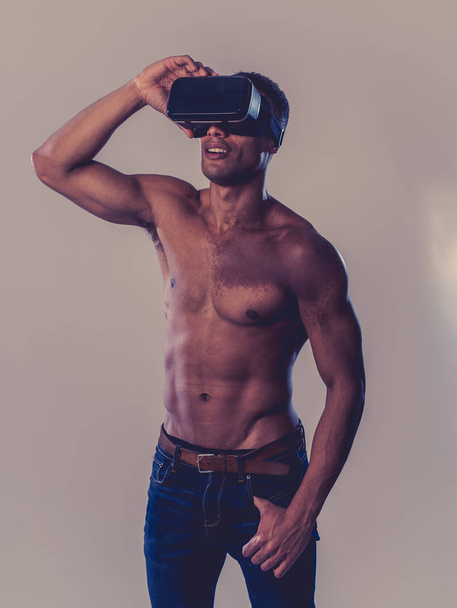 Attractive strong muscular african man using augmented VR glasses, feeling excited about simulation exploring new experiences. In virtual reality, virtual workout and new technology concept. - 写真・画像