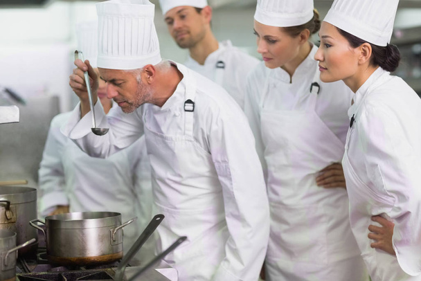 Head chef tasting a soup while staff watch in a commercial kitchen - Photo, Image