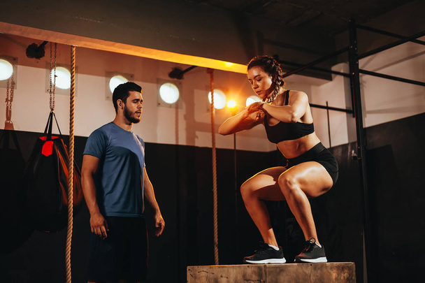 Fit young woman doing a box jump exercise. Sports woman doing a box squat at the gym - Photo, Image