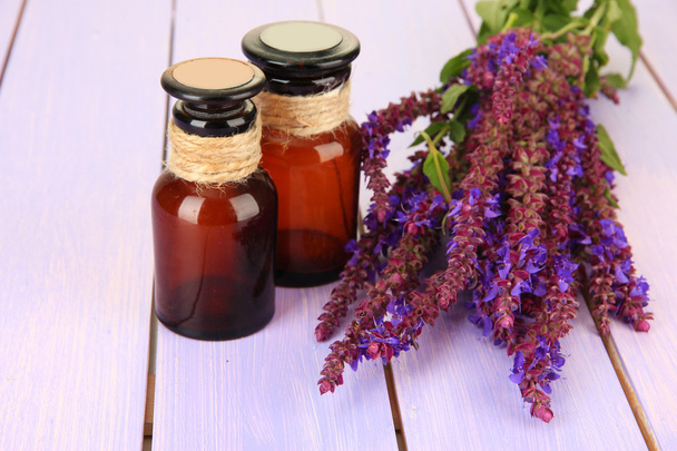 Bottiglie di medicina e fiori di salvia su sfondo di legno viola
 - Foto, immagini