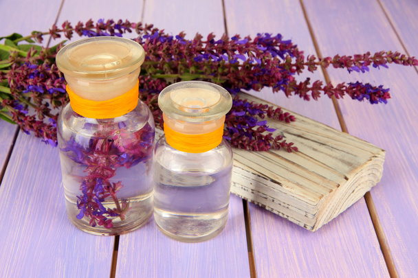 geneeskundeflessen met salvia bloemen op paarse houten achtergrond - Foto, afbeelding