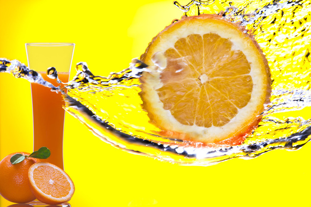 Blick auf ein Orangenstück, das bespritzt wird und ein Glas Saft auf dem Rücken - Foto, Bild