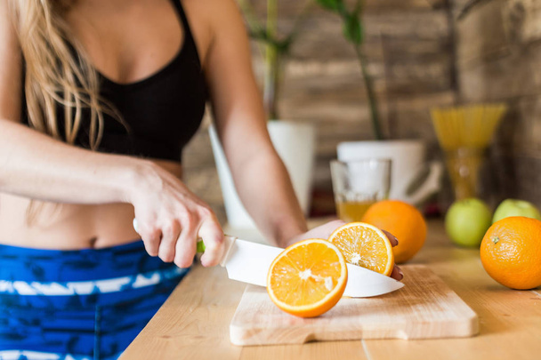 Attractive girl in sportswear preparing a healthy breakfast in the kitchen before training, cutting fruit and making fresh juice. Healthy lifestyle, fitness and beaut - Foto, Bild