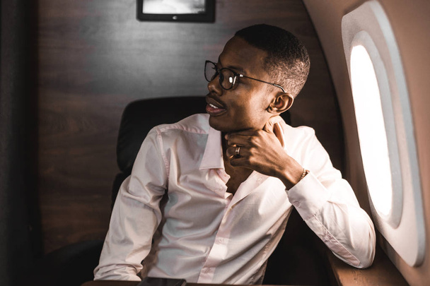 Successful young Afro American black businessman sitting in the chair of his private jet - Foto, afbeelding
