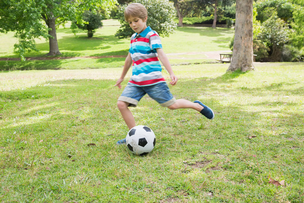 Full length of a young boy kicking ball at the park - Фото, изображение