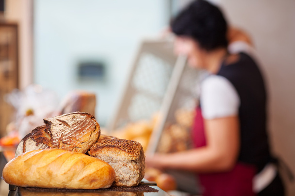 Bread Loafs On Counter With Woman Empting Create In Background - Fotoğraf, Görsel