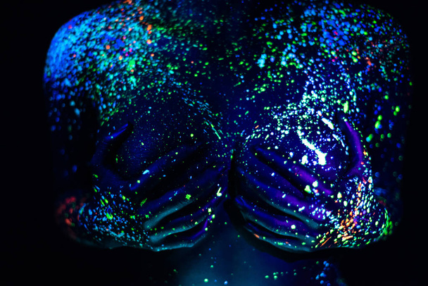 Ultraviolet body art blue night sky with stars. Fluorescent paint on a large female breast covered with hands. - Foto, imagen