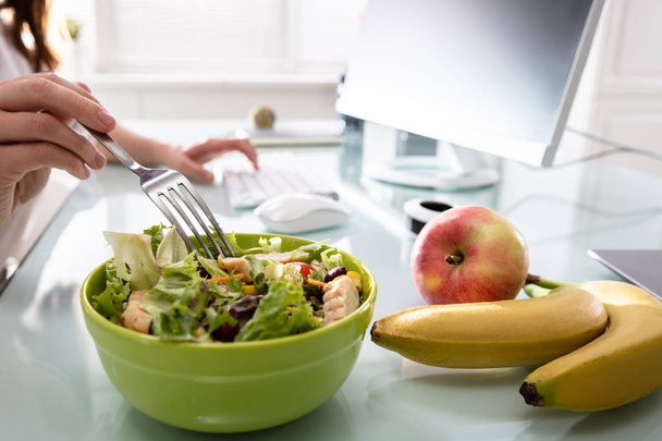 Lähikuva naisen käsi tilalla haarukka, kun ottaa terveellisen salaatin Office Desk
 - Valokuva, kuva