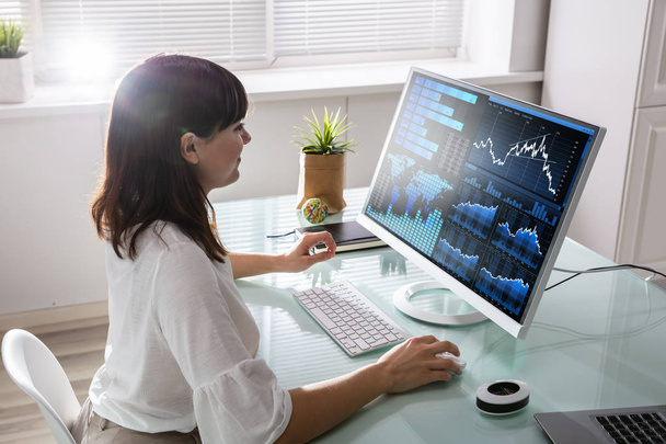 Young Female Stock Market Broker Analyzing Graph On Computer At Workplace - Foto, Bild