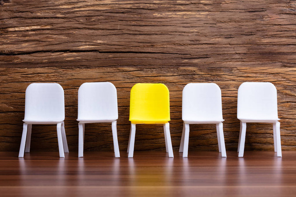 Miniatuur stoel in een rij met een gele in het midden op houten achtergrond - Foto, afbeelding