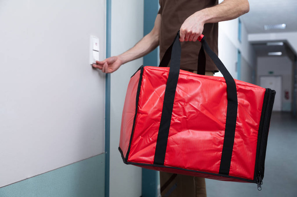 Pizza Delivery Man Ringing The Door Bell With A Large Red Bag In His Hand - 写真・画像