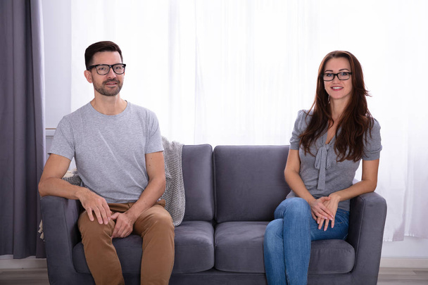 Young Couple Sitting On Sofa Looking At Each Other - Фото, зображення