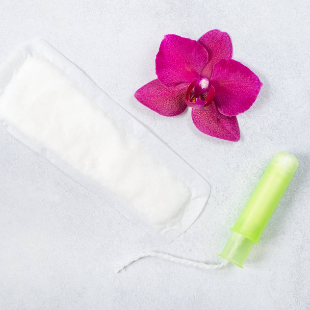 Cotton tampon, menstrual pad with orchid on light grey background. Concept of critical days, menstruation or womans health. Top view, flat lay. - Fotoğraf, Görsel