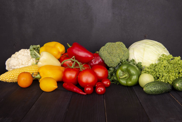 A composition of fresh vegetables on a wooden black table. Tasty colored vitamins on a dark background. A group of useful products. Copy space.  - Foto, imagen