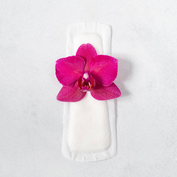 Menstrual pad with orchid on light grey background. Concept of critical days, menstruation or womans health. Top view, flat lay. - Photo, Image