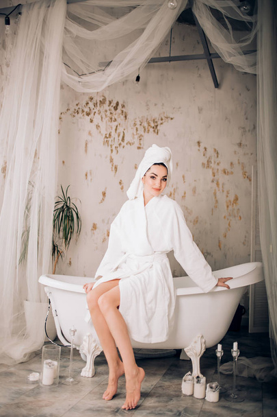 Attractive girl wearing white bathrobe and towel on head in bathroom - Фото, зображення