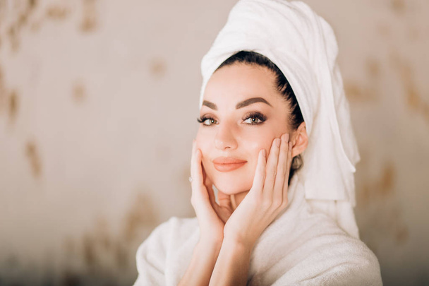 Attractive girl wearing white bathrobe and towel on head in bathroom - Foto, afbeelding
