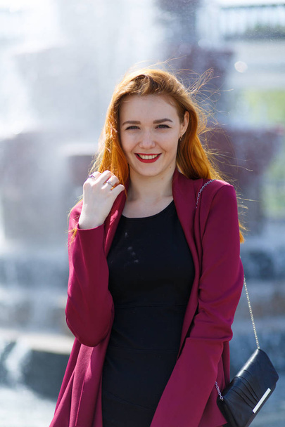 Young girl with red hair on the background of unfocused fountain. - Foto, immagini