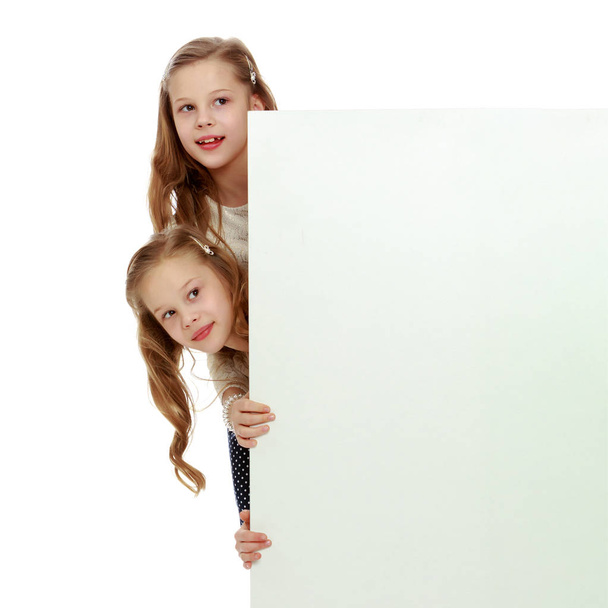 Two little girls peeking out from behind a white advertising ban - Foto, afbeelding