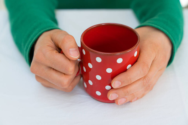 Beyaz noktalı kırmızı kahve fincanı tutan bir kadın.  - Fotoğraf, Görsel
