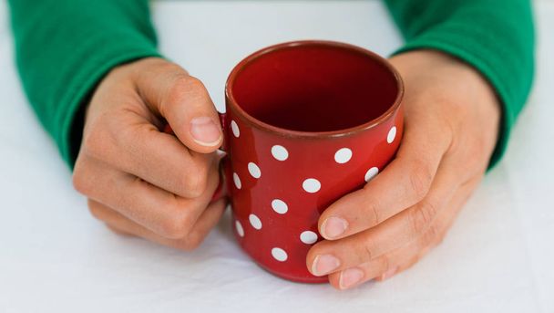 nő kezében egy piros kávé csésze fehér polka pontok egy fehér  - Fotó, kép