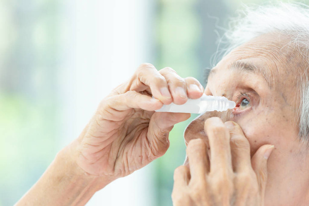Asian senior woman putting eye drop,closeup view of elderly  person using bottle of eyedrops in her eyes,sick old woman suffering from irritated eye,optical symptoms,health concept - Photo, Image