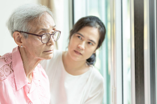 Mulher idosa com sintomas depressivos precisa de cuidados estreitos, asiático jovem cuidador apoio, Alzheimer paciente
 - Foto, Imagem