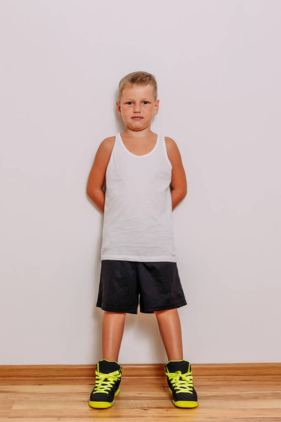 seven-year-old boy in a white t-shirt, black basketball shorts and sneakers on a white background - Fotó, kép