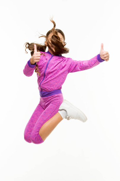 This child is active. Active little girl gesturing thumbs ups in motion isolated on white. Small child jumping in active sportswear. Fit and energetic kid. Getting more active and energetic - Φωτογραφία, εικόνα