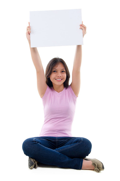 Southeast Asian young girl arms raised holding a white card board sitting over white background - Фото, изображение