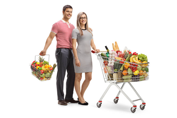 Young couple with a full shopping cart and a shopping basket isolated on white background - Photo, Image