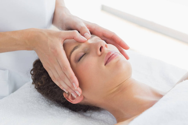 Closeup of beautiful woman receiving massage on forehead in health spa - Photo, image