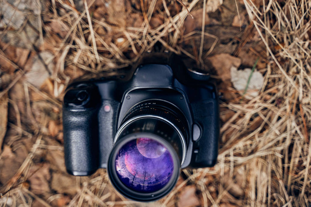                                digital camera lies on dry grass and in its lens reflects the purple landscape: forest, trees and sky - Photo, Image