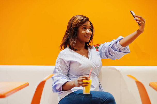 African woman sitting on cafe against orange wall with pineapple - Foto, imagen