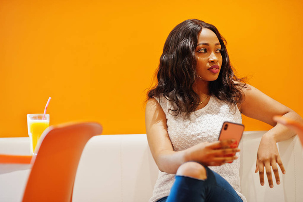 African woman sitting on cafe against orange wall with pineapple - Photo, Image