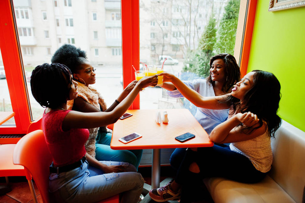 Four young african girls cheers with orange juices while sitting - Foto, imagen
