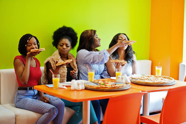 Quatro jovens meninas africanas em restaurante colorido brilhante comendo piz
 - Foto, Imagem