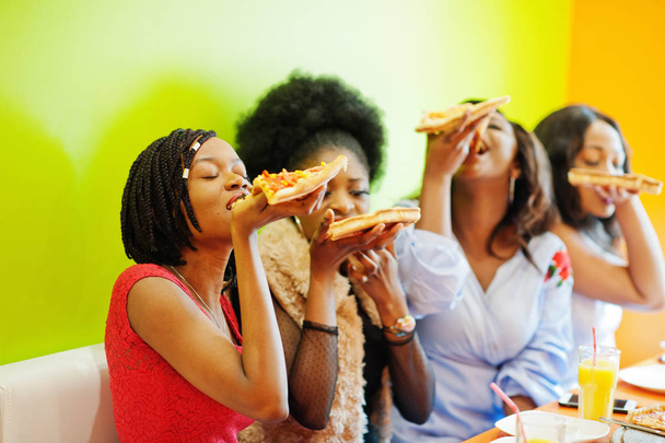 Parlak renkli restoranda dört genç Afrikalı kız piz yemek - Fotoğraf, Görsel