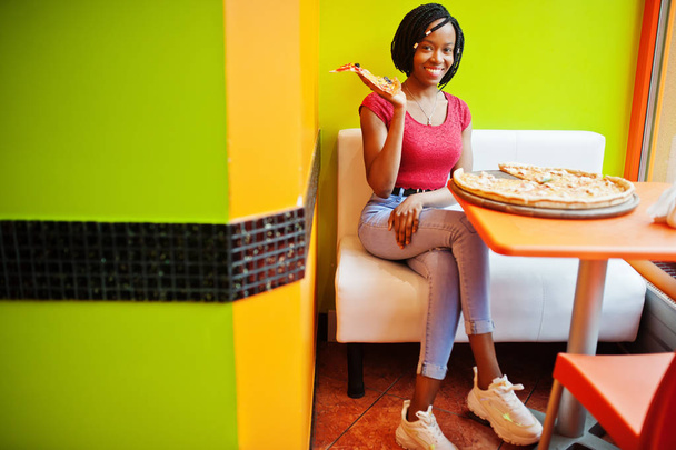 African woman with pizza sitting at bright colored restaurant. - Foto, afbeelding