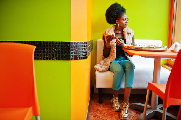 African woman with pizza sitting at bright colored restaurant. - Фото, зображення